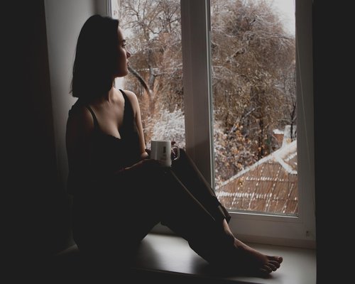 woman resting eyes looking out of window in apartment